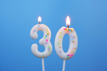 Burning white birthday candles on blue background, number 30.
