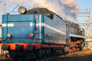 A steam locomotive carrying coal departs from the station