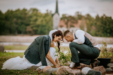 A bride and groom joyfully plant a tree together as a symbolic wedding ritual, representing love,...
