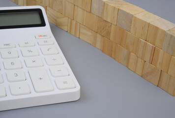 Wall made of wooden cubes and calculator on gray background. Cost of safety and protection concept.