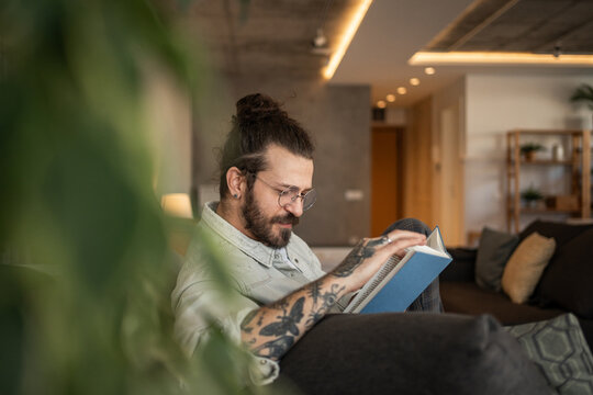 Young man reading a book at home on the sofa