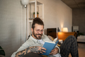 Smiling man reading a book at home on the sofa