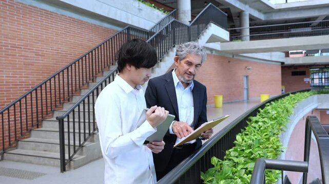 Asian senior professor is giving advice  to the college student on the research thesis while walking in the university faculty campus for education, academic and business concept