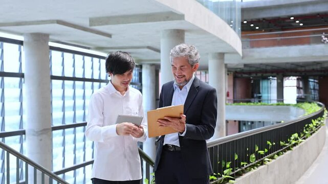 Asian senior professor is giving advice  to the college student on the research thesis while walking in the university faculty campus for education, academic and business concept