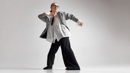 Low angle photo of young woman, dressed stylish oversized formal attire and dancing shows freedom and individuality, against white studio background. Concept of business success, motivation. © Lustre Art Group 