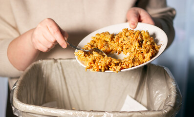 Woman holding food plate and throwing away food leftovers using spoon into garbage bin trash. Compost from leftover food. Stop Food Waste Day