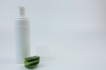Close-up of a white foam cleanser with a dispenser for nourishing, moisturizing and cleansing the skin stands on a white background, next to it there are aloe leaves with space for text. Body and face