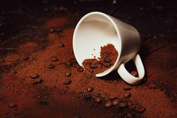 Dark temptation. coffee beans and ground coffee on the table and a white cup lying sideways