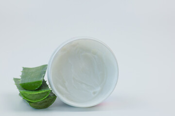 Close-up of an open round jar of cream for nourishing and moisturizing the skin stands on a white background, aloe leaves lie nearby. Body and face care concept, skin care, cosmetics with aloe extract