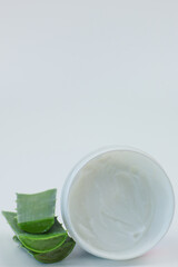 Close-up of an open round jar of cream for nourishing and moisturizing the skin stands on a white background, aloe leaves lie nearby. Body and face care concept, skin care, cosmetics with aloe extract