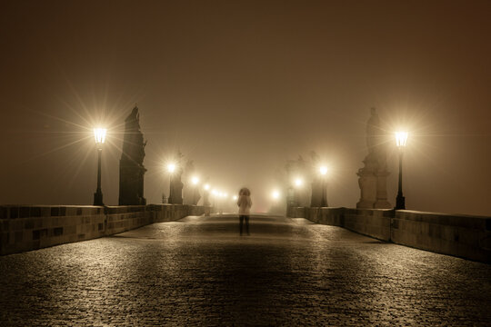 View of Charles Bridge shrouded in fog with illuminated lamp posts and cobblestone pathway, Prague, Bohemia, Czechia.