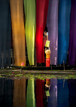 Inle Lake, Myanmar - 14 November 2019: View of mother and child in a boat with vibrant drying cloth and colorful handmade fabric, Inle Lake, Shan State, Myanmar.