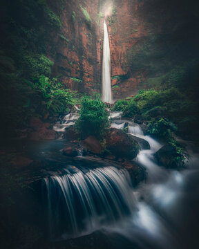 View of Kapas Biru waterfall cascading through lush green forest with rocks and a serene stream, Pronojiwo, Lumajang, East Java, Indonesia.