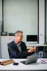 Confident businessman working on finance analysis with a tablet and laptop at office desk. Perfect...