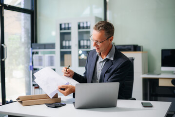 Confident businessman working on finance analysis with a tablet and laptop at office desk. Perfect for business