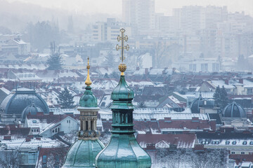 View of a beautiful aerial cityscape featuring a historic church tower and dome in winter with snowy rooftops, Graz, Styria, Austria.