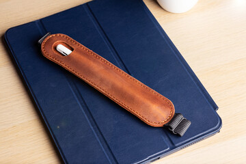 Handmade brown leather case for a stylus lies on a tablet in a blue case. Stylus and tablet on a...