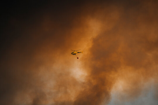 View of dramatic aerial scene of helicopter battling wildfire with intense smoke and dark clouds, Cueva del Viento, Santa Cruz de Tenerife, Spain.