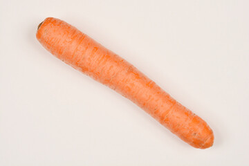 A top-down shot of a single whole carrot lying diagonally on a light-colored surface, showcasing its orange color and textured skin