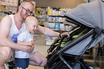Obraz premium Happy little kid together with his father choosing a baby troller in a children shop. 