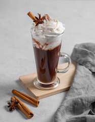 Hot chocolate with whipped cream, cinnamon and spices in a tall glass on a light background.