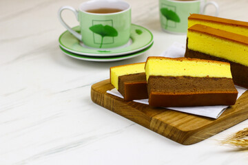 Lapis Surabaya or Indonesian layered sponge cake on wooden chopping board with cups of tea. White marble background.