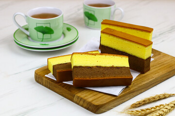 Lapis Surabaya or Indonesian layered sponge cake on wooden chopping board with cups of tea. White marble background.