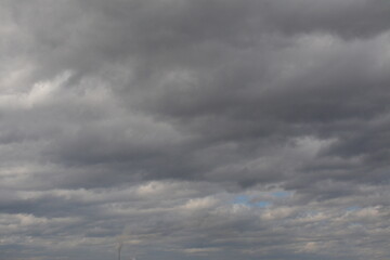 Cloudy sky with thick clouds. A small pipe with smoke on the distant horizon