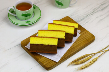 Lapis Surabaya or Indonesian layered sponge cake on wooden chopping board with cups of tea. White marble background.