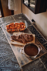 Sliced roast beef on a cutting board stands next to a baked sweet potato in a glass dish on the table