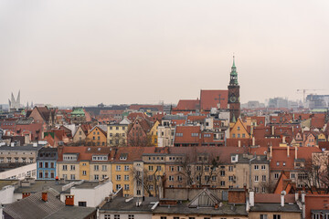 Obraz premium Picturesque aerial view of European old town with colorful historic buildings, red rooftops, and tall clock tower on cloudy day. Mix of medieval and modern architecture in an urban landscape.