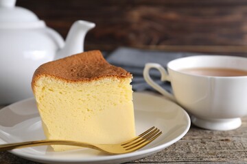 Piece of tasty Japanese Castella sponge cake, tea and fork on wooden table, closeup