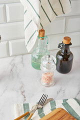 Kitchen utensils - cutting board, cutlery, vegetable oil, salt and spices with grinders and towels on a light background