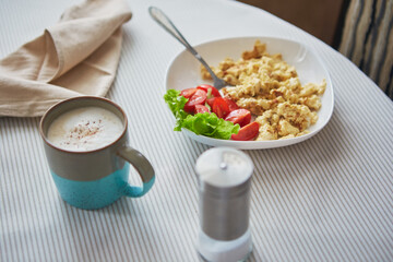 Breakfast table. Cup of coffee and plate with scrambled eggs and vegetables on the table