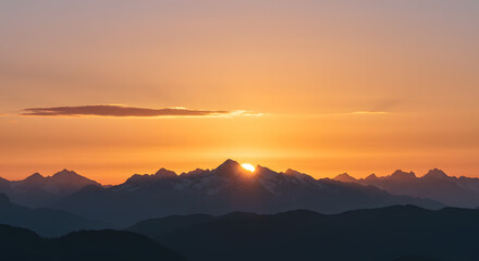 A golden sunset behind the mountains, with soft clouds glowing in the evening light.
