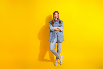 Fashionable young woman in denim and beanie posing against vivid yellow background, showcasing casual style and charming personality