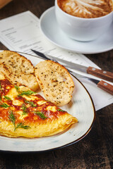 Omelet with two pieces of fried baguette and cup of cappuccino on the table