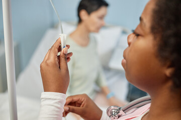 Medical professional preparing IV drip for patient lying in hospital bed, focusing on medical care...