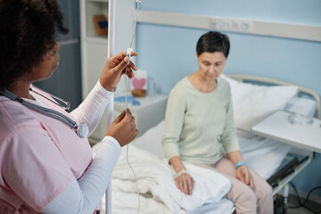 Nurse adjusting IV drip for a female patient resting in a hospital bed during medical treatment session. Nurse focusing on providing essential care for patient in medical facility