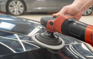 Car detailing series: Polishing black car close-up. The process of polishing the car body in...