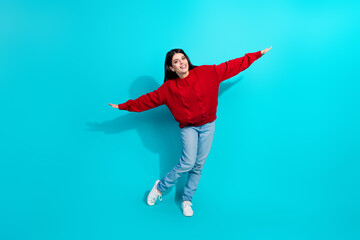 Trendy Young Woman in Red Knit Sweater Posing Playfully Against Teal Background Showcasing Modern Fashion Style and Cheerful Personality