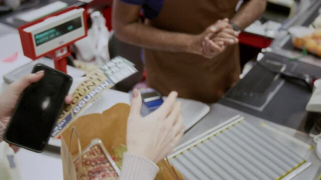 Closeup of unrecognizable cashier handing bonus discount coupons to customer buying groceries in supermarket