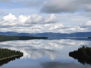 Fototapeta premium Clouds Reflecting on a Calm Lake Surrounded by Forest and Mountains in the Distance