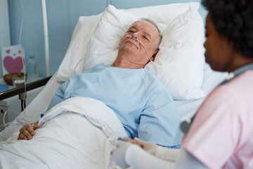 Elderly man lying in hospital bed with attendant nearby discussing medical details, sharing empathy...