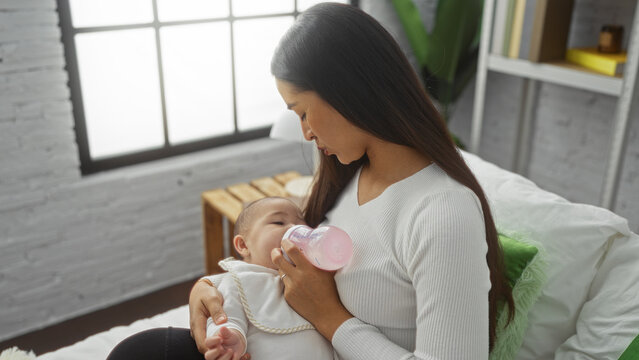 Woman feeding baby with bottle in cozy bedroom setting, symbolizing love and family bonding indoors at home, emphasizing the nurturing role of a mother and daughter.