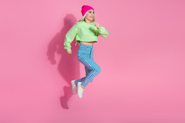Stylish young woman jumps joyfully against a vibrant pink background wearing trendy casual clothes...