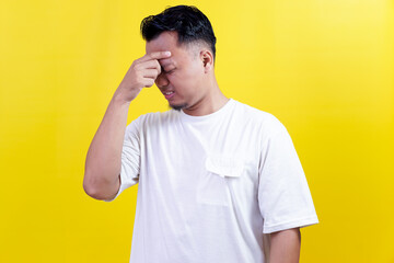 An asian man holding his forehead in pain, expressing discomfort, possibly due to headache or...