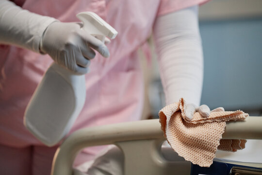 Hospital staff member cleaning hospital bed using disinfectant spray and cloth ensuring sanitation and safety during patient care