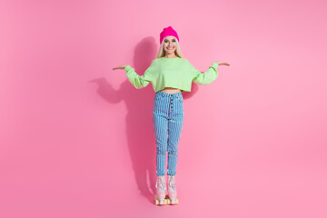 Young blonde woman in vibrant outfit and roller skates posing with friendly gestures on a pink background, full of charm and energy.