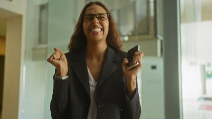 Woman celebrating success in office holding phone wearing suit joyful expression